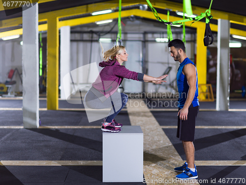 Image of woman working out with personal trainer jumping on fit box