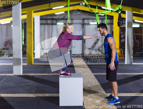 Image of woman working out with personal trainer jumping on fit box