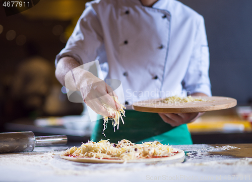 Image of chef sprinkling cheese over fresh pizza dough