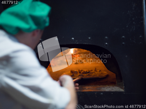 Image of chef putting delicious pizza to brick wood oven