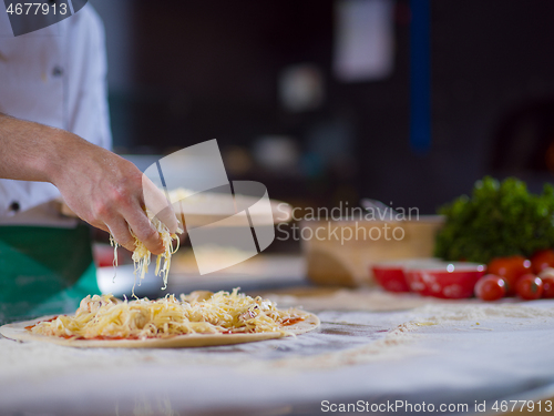 Image of chef sprinkling cheese over fresh pizza dough