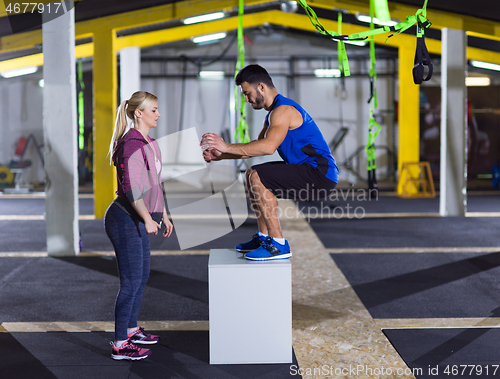 Image of woman working out with personal trainer jumping on fit box