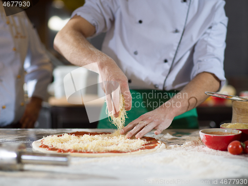 Image of chef sprinkling cheese over fresh pizza dough