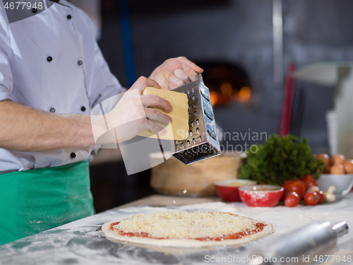 Image of chef sprinkling cheese over fresh pizza dough