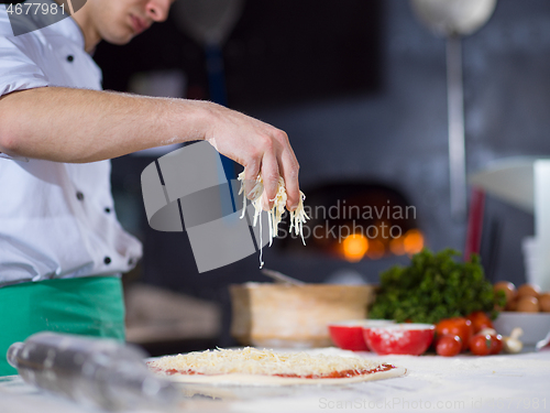 Image of chef sprinkling cheese over fresh pizza dough