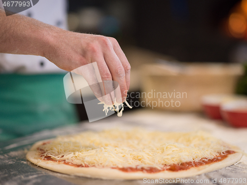 Image of chef sprinkling cheese over fresh pizza dough