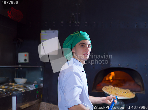 Image of chef putting delicious pizza to brick wood oven