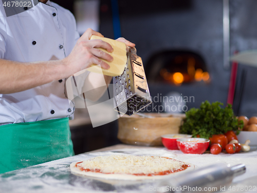 Image of chef sprinkling cheese over fresh pizza dough