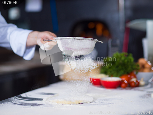 Image of chef sprinkling flour over fresh pizza dough