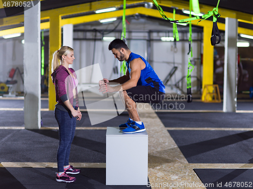 Image of woman working out with personal trainer jumping on fit box