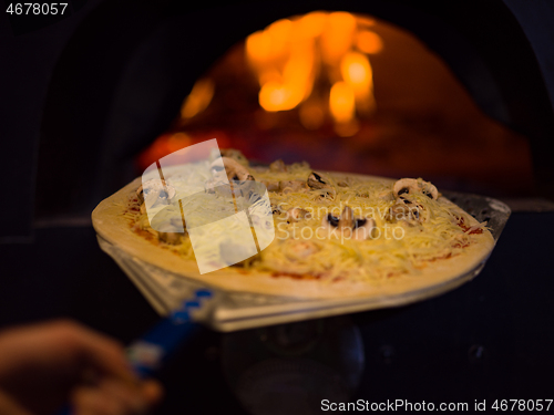 Image of chef putting delicious pizza to brick wood oven