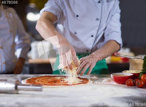 Image of chef sprinkling cheese over fresh pizza dough