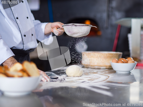 Image of chef sprinkling flour over fresh pizza dough