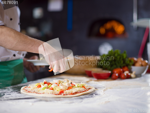 Image of chef putting fresh vegetables on pizza dough