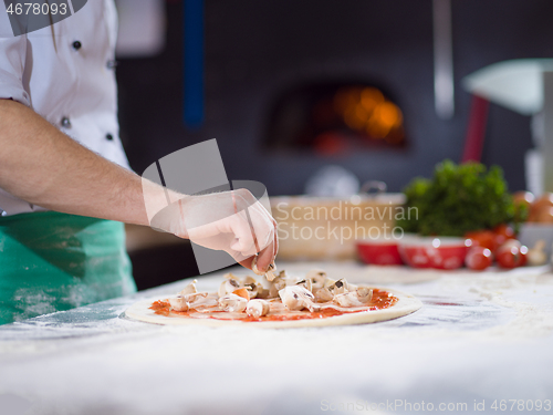 Image of chef putting fresh mushrooms on pizza dough