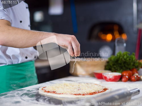 Image of chef sprinkling cheese over fresh pizza dough