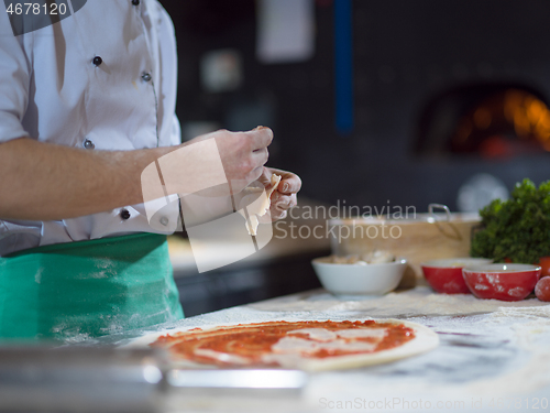 Image of chef putting cut sausage or ham on pizza dough