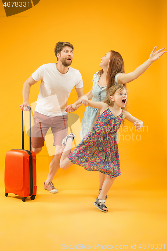 Image of Happy parents with daughter and suitcase at studio isolated on yellow background