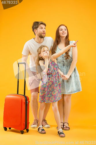 Image of Happy parents with daughter and suitcase at studio isolated on yellow background