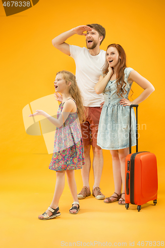 Image of Happy parents with daughter and suitcase at studio isolated on yellow background