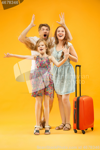 Image of Happy parents with daughter and suitcase at studio isolated on yellow background