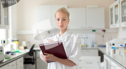 Image of Portrait of young, confident female health care professional taking notes during inventory in scientific laboratory or medical doctors office