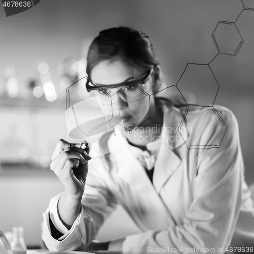 Image of Portrait of a confident female researcher in life science laboratory writing structural chemical formula on a glass board.