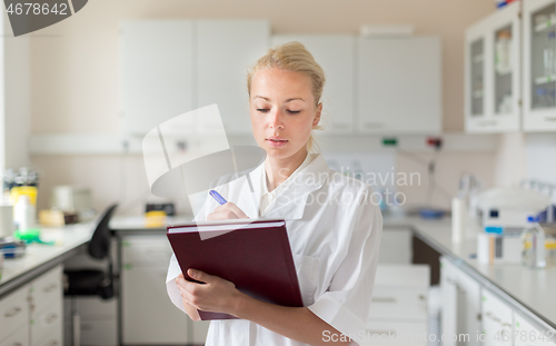 Image of Portrait of young, confident female health care professional taking notes during inventory in scientific laboratory or medical doctors office