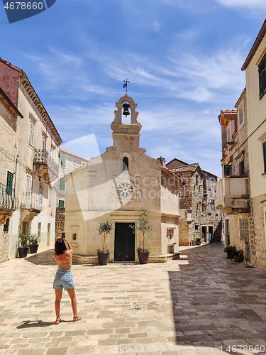 Image of Female tourist taking photo of mall church on square of small urban village of Stari grad on Hvar island in Croatia, Adriatic Sea, Europe