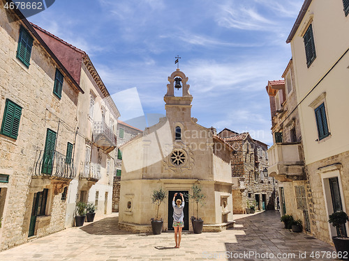 Image of Female tourist taking photo of mall church on square of small urban village of Stari grad on Hvar island in Croatia, Adriatic Sea, Europe