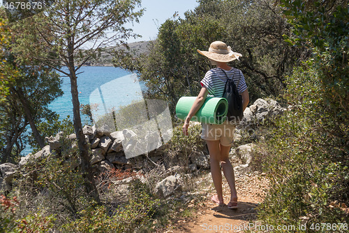 Image of Young active feamle tourist wearing small backpack walking on coastal path among pine trees looking for remote cove to swim alone in peace on seaside in Croatia. Travel and adventure concept