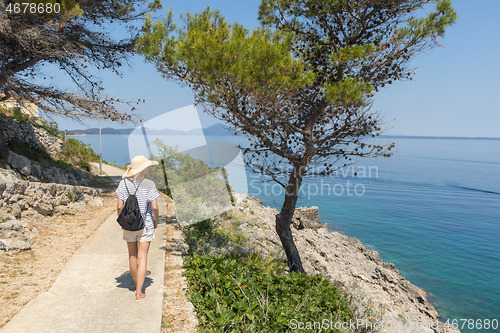 Image of Young active feamle tourist wearing small backpack walking on coastal path among pine trees looking for remote cove to swim alone in peace on seaside in Croatia. Travel and adventure concept