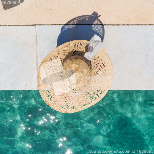 Image of Woman wearing big summer sun hat relaxing on pier by clear turquoise sea.