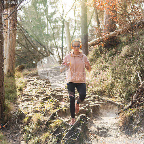 Image of Active sporty woman listening to the music while running in autumn fall forest. Female runner training outdoor. Healthy lifestyle image of young caucasian woman jogging outside