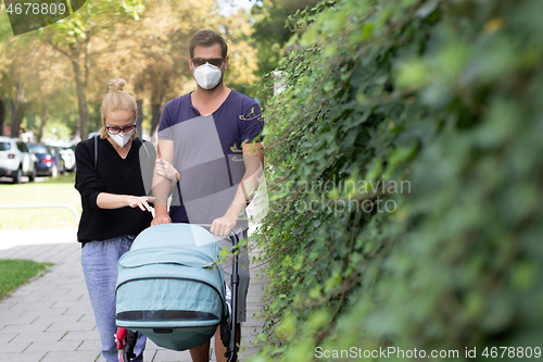 Image of Worried young parent walking on empty street with stroller wearing medical masks to protect them from corona virus. Social distancing life during corona virus pandemic