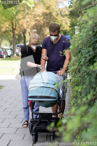 Image of Worried young parent walking on empty street with stroller wearing medical masks to protect them from corona virus. Social distancing life during corona virus pandemic