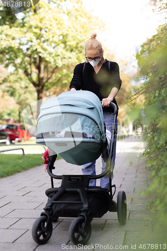 Image of Worried young mom walking on empty street with stroller wearing medical masks to protect her from corona virus. Social distancing life during corona virus pandemic