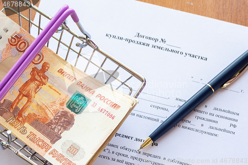 Image of There is a bundle of money in a grocery basket and a ballpoint pen on the land purchase agreement