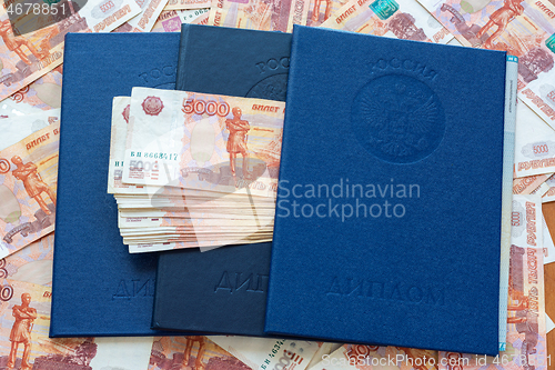 Image of Three blue higher education diplomas lie in the background from the money, a bundle of money sticks out between the diplomas