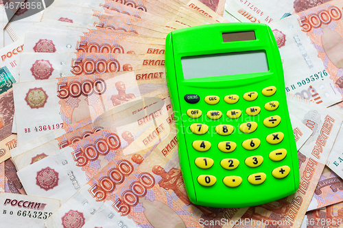 Image of A green calculator lies on a stack of five thousandth bills spread out in a fan.