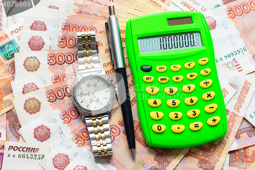 Image of Against the background of Russian five-thousandth bills lies a calculator with the number one million, a watch and a pen