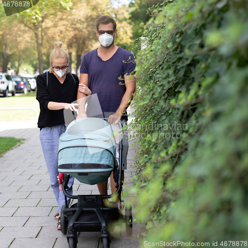 Image of Worried young parent walking on empty street with stroller wearing medical masks to protect them from corona virus. Social distancing life during corona virus pandemic