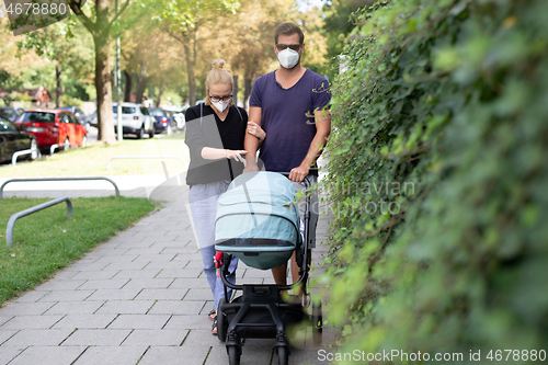 Image of Worried young parent walking on empty street with stroller wearing medical masks to protect them from corona virus. Social distancing life during corona virus pandemic