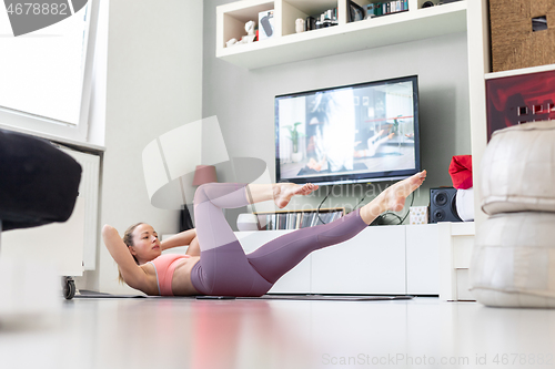 Image of Attractive sporty woman working out at home, doing pilates exercise in front of television in her small studio appartment. Social distancing. Stay healthy and stay at home during corona virus pandemi