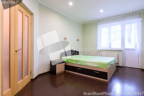 Image of Bedroom interior with a bed in the middle and a large window opening onto a balcony