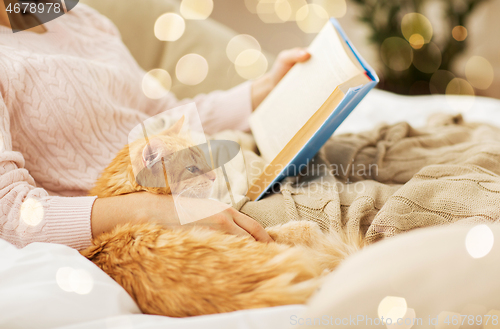 Image of red cat and female owner reading book at home