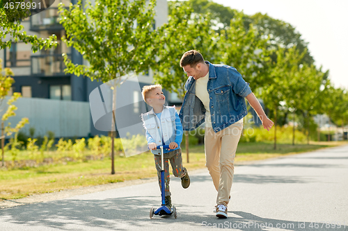 Image of happy father and little son riding scooter in city