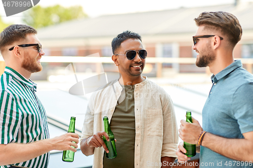 Image of happy male friends drinking beer at rooftop party