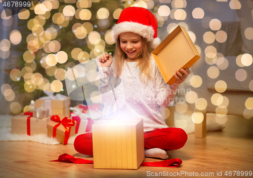 Image of excited girl in santa hat opening christmas gift