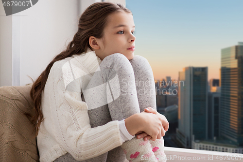 Image of sad girl sitting on sill at home window over city